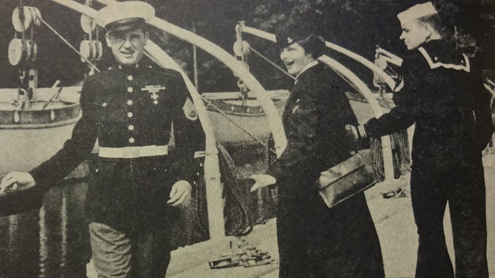 An image that looks strikingly similar to the infamous distracted boyfriend meme. An old photo in sepia colours from the 1950s. On the right, a male Navy cadet walks with his arm around a woman also dressed in Navy attire. She has her head turned and is reaching out to an impeccably-dressed man in Marine Corps dress blues. The man looks outrageously confident.