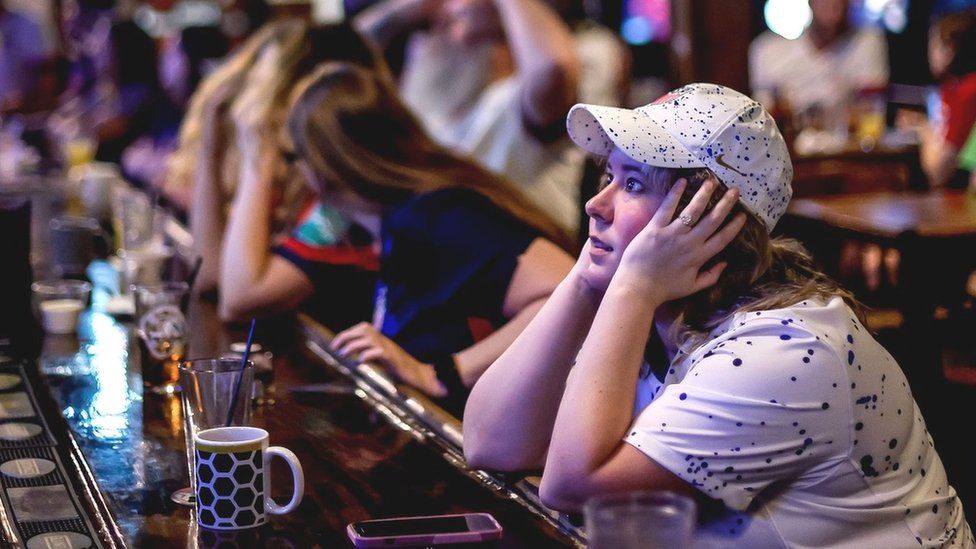 A woman with head in her hands at a bar reacts to the USA's loss to Sweden in a brewhouse in Georgia