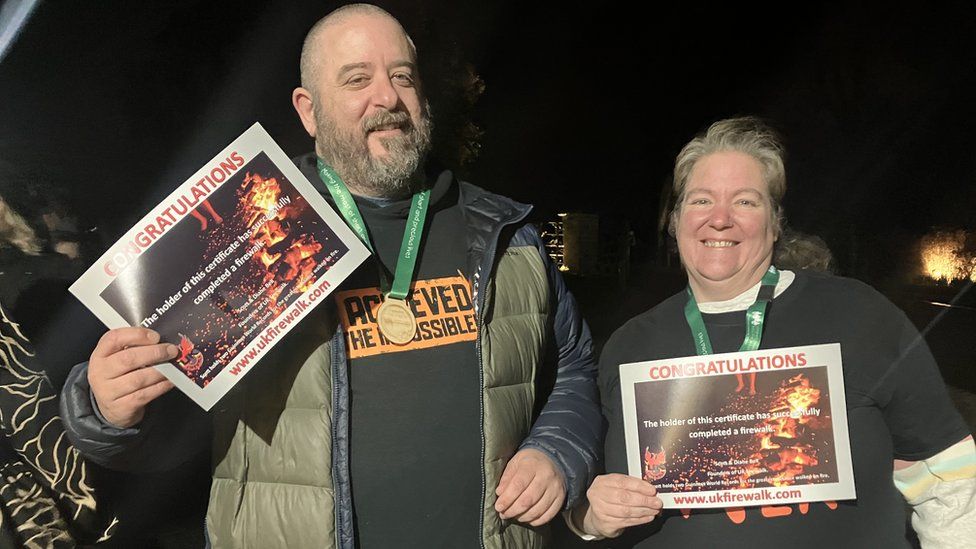 A man and a woman holding certificates showing their completion of the fire walk