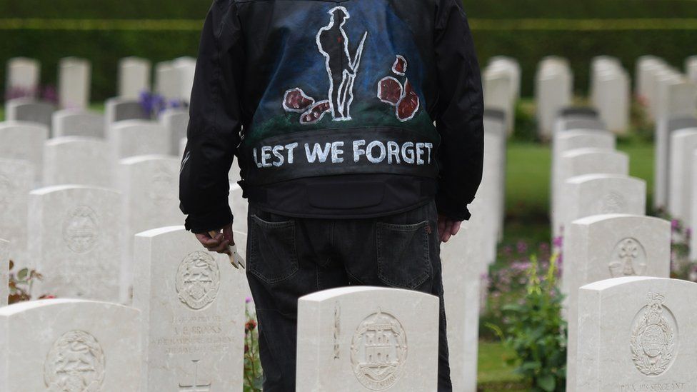 A person stands in a jacket reading 'lest we forget' at a Commonwealth War Graves Commission event in Bayeux, Normandy, France, in 2019.