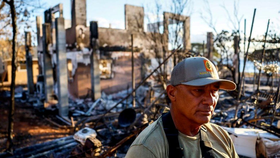 A man sits in his backyard that abuts a home that was destroyed in the fire