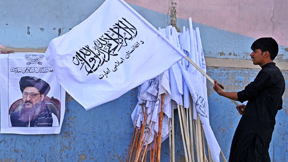 A vendor holds a Taliban flag next to a poster of Taliban leader Abdul Ghani Baradar as he waits for customers along a street in Kabul on August 27, 2021.