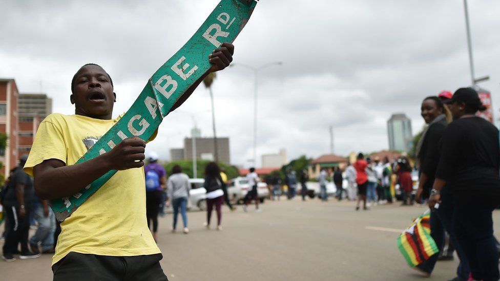 A man reacts with a sign reading 'Robert Mugabe Road' during a demonstration marching towards the State House while demanding the resignation of Zimbabwe's president on November 18, 2017 in Harare