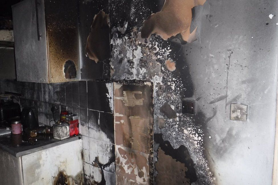A wall and cupboards blackened by smoke in a kitchen