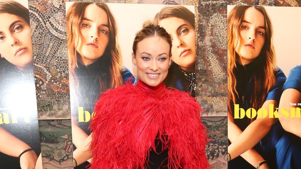 Booksmart director Olivia Wilde standing in front of posters for the film