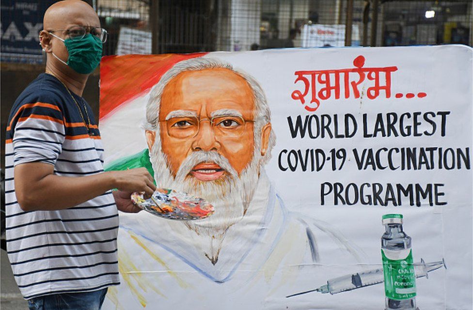 An artist paints Mr Modi's face on a vaccination programme banner