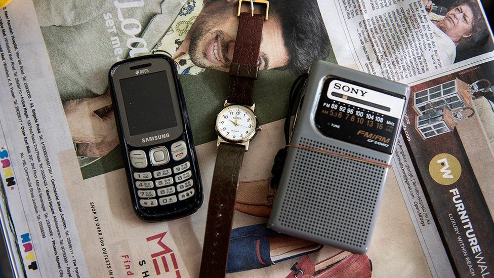 A mobile phone, a watch and a radio transmitter lying on a newspaper in a room at the care home