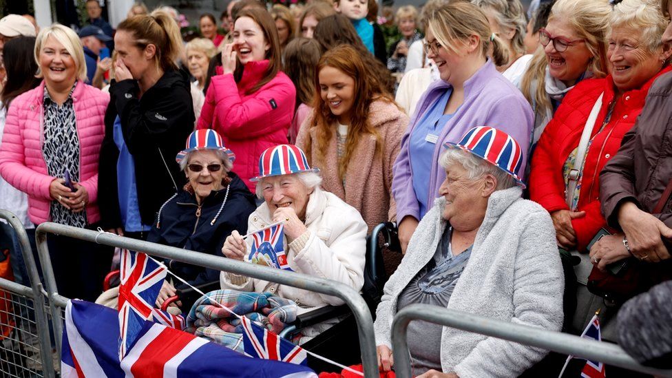 Three elderly women - wearing Union flag hats and holding flags - wait outside Hillsborough Castle ahead of the visit by the King and Camilla