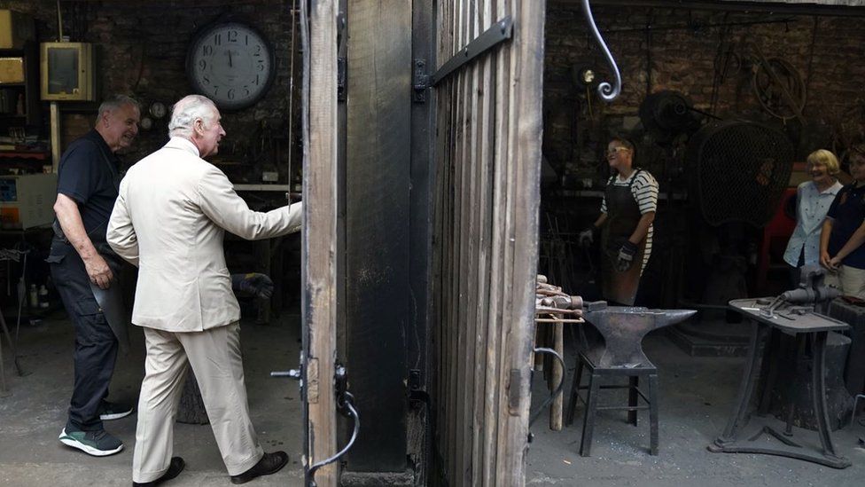 The Prince of Wales is shown around a forge by Rex Latham (left) during a visit to Cockington Court in Torquay