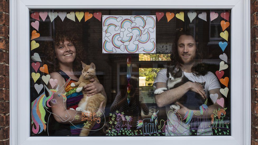 Two people holding two cats in a window in Bedford