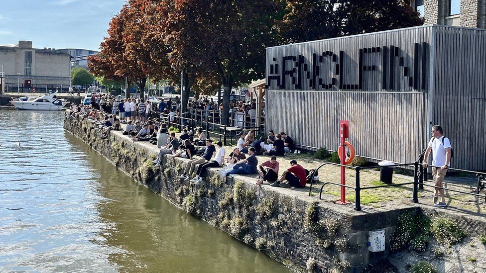 People sitting on the harbourside in Bristol in the sunshine outside the Arnolfini bar