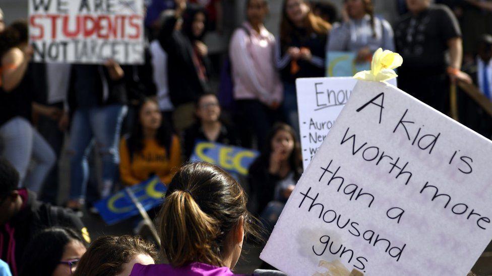 Denver high school students holding up protest signs including "a kid is worth more than a thousand guns".