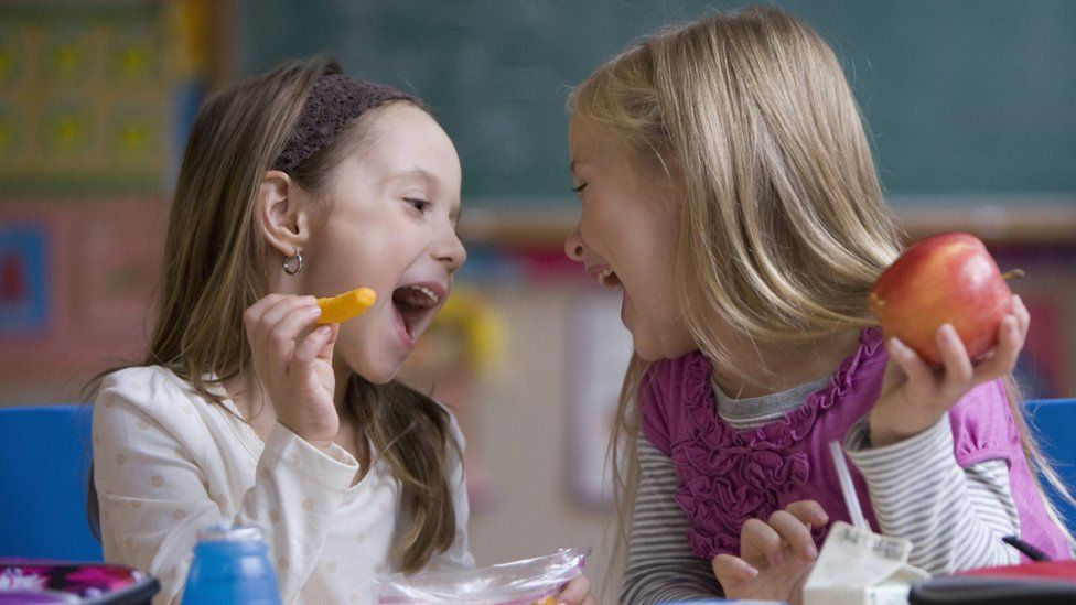 Two school girls eating food in a school