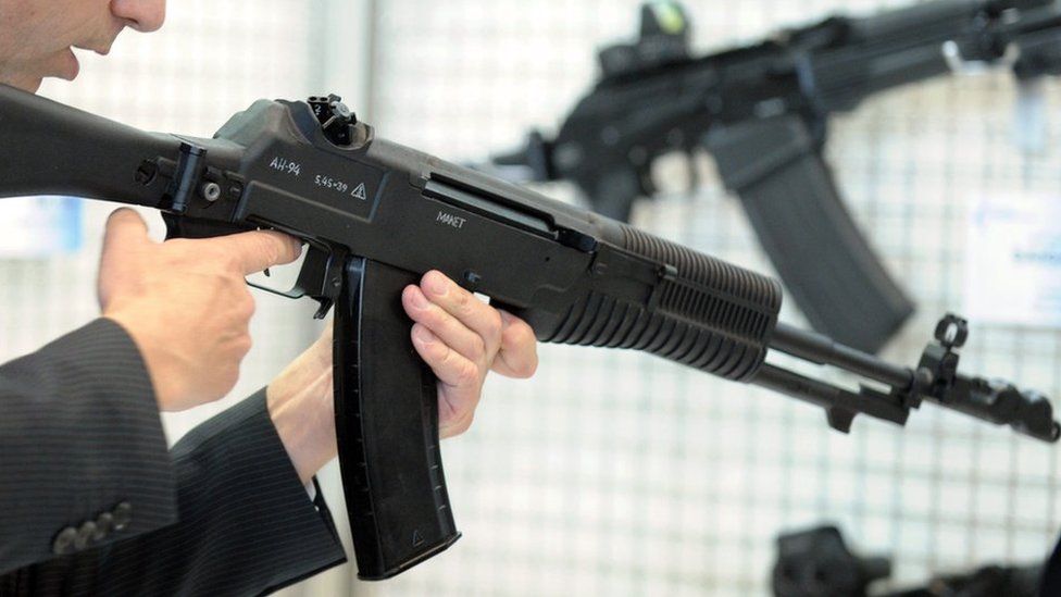 A man holding a Kalashnikov rifle at a trade exhibition