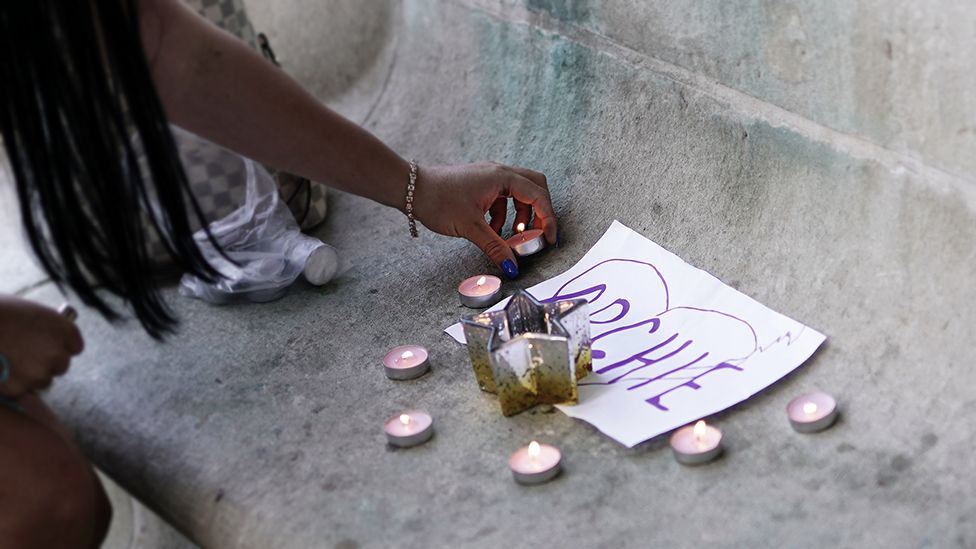 Candles being placed next to piece of paper with Archie written on it inside a hand-drawn heart, outside the Royal London Hospital