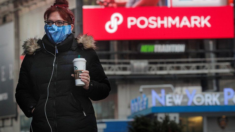 A woman walks through Times Square as a screen displays the company logo for Poshmark Inc. during it"s IPO at the Nasdaq Market Site in Times Square in New York City, U.S., January 14, 2021.
