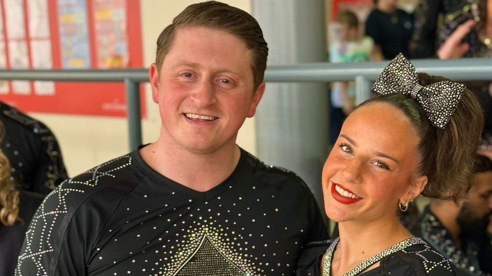Matthew Delday and Caitlin Pretious smiling at the camera, they are both wearing sparkly cheerleading outfits