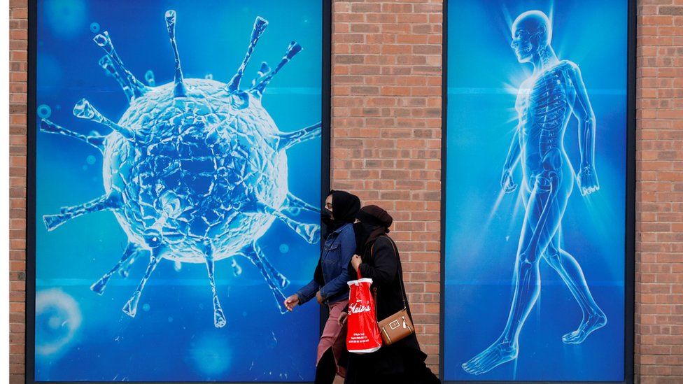 Two women walk past an illustration of a virus in Oldham
