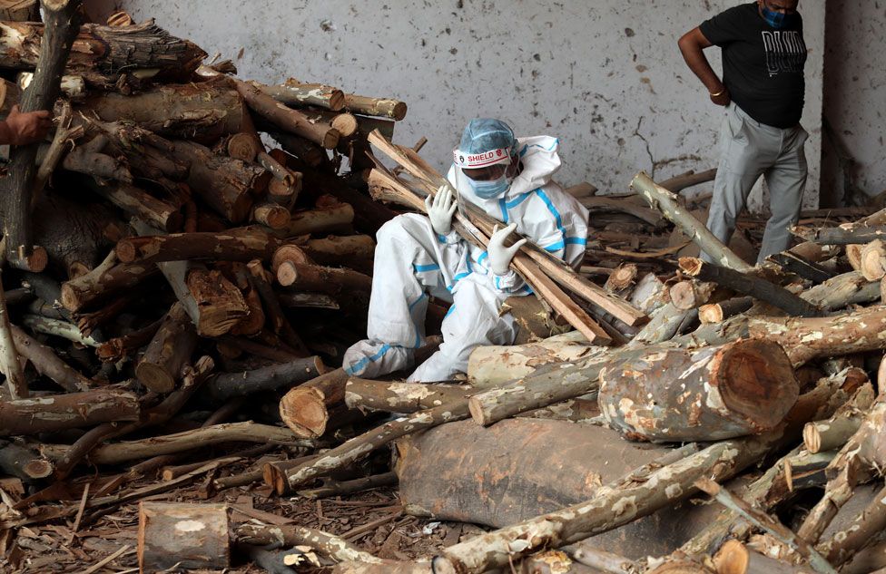 A person sits on the ground clutching wood at a cremation ground in New Delhi, India