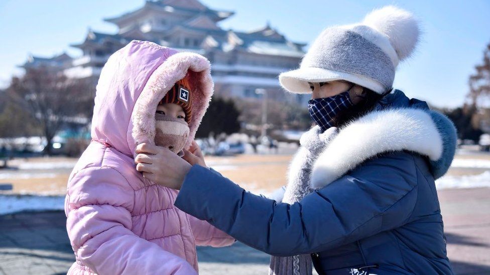 A woman helps her daughter seen wearing a face mask in Pyongyang