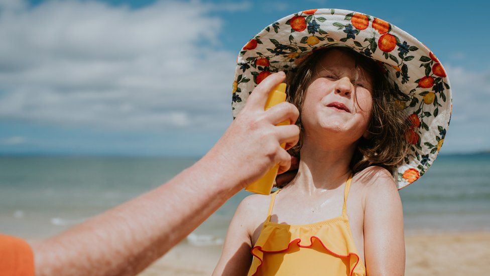 A little girl wearing a sun hat has sun cream applied to her face