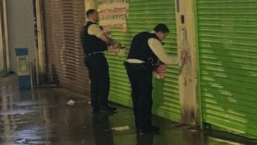 Two officers removing hostage posters from business shutters in Edgware
