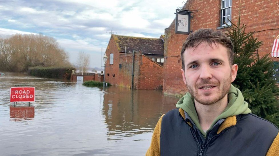 Man stood looking at the camera with loads of floodwater behind