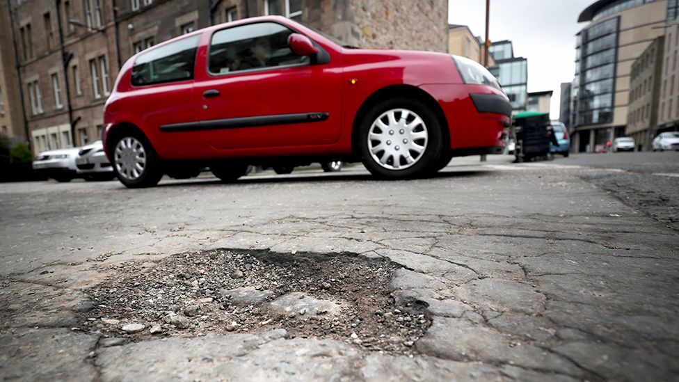 A pothole in a road with a red car in the background
