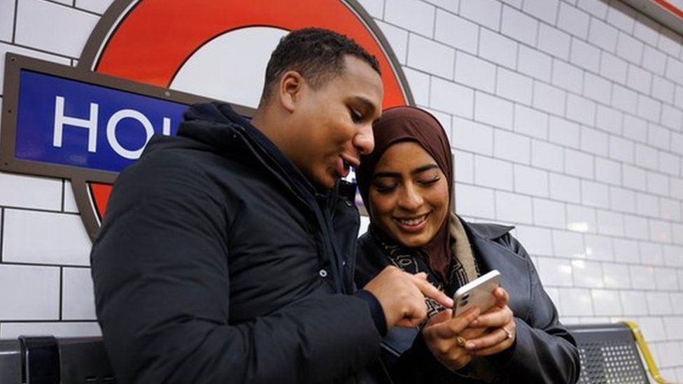 A man and a woman using a phone in a Tube station