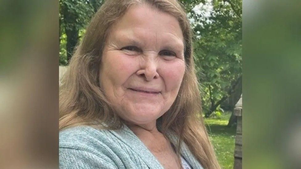 Christine Emmerson pictured with long light brown hair standing in front of trees