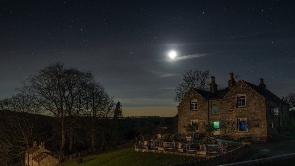 Moon and stars lighting up a dark night sky above a house and tree in the countryside