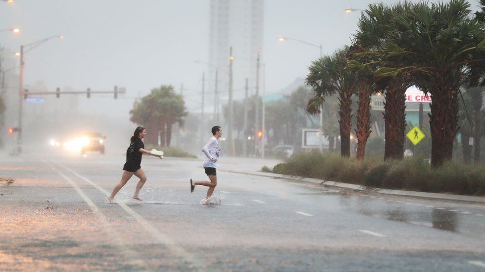 People run across a road through the rain and wind as the outer bands of Hurricane Sally come ashore on September 15, 2020 in Gulf Shores, Alabama