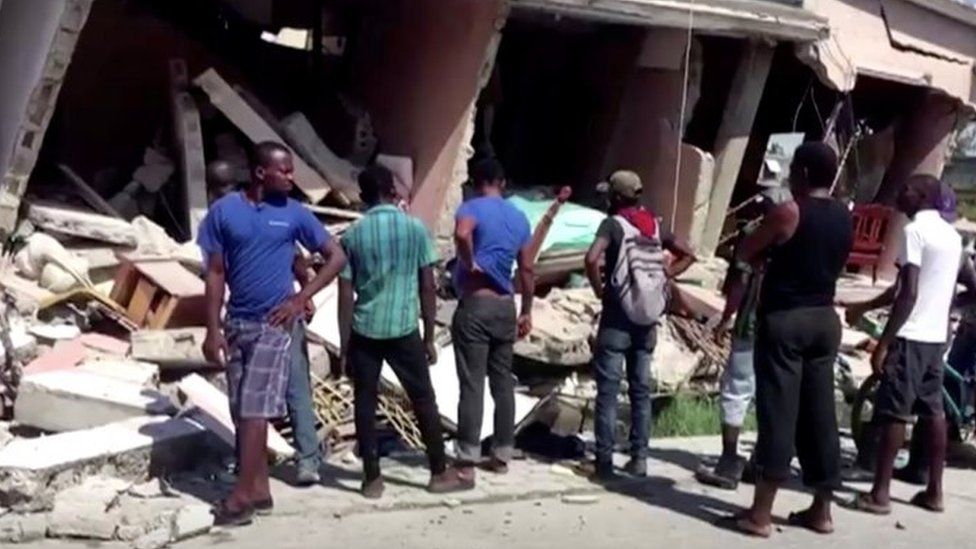 People stand in front of a collapsed building following an earthquake
