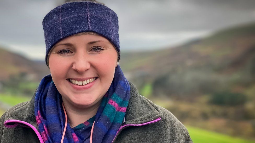 Katie-Rose Davies wearing a wool cap and heavy coat standing in a mountain farm area
