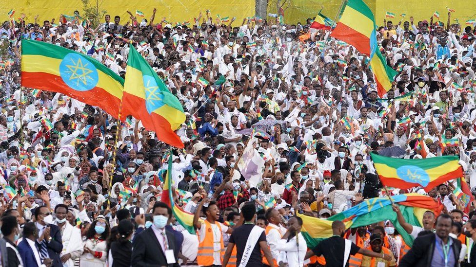 Large crowd of Ethiopians celebrating with some people carrying giant Ethiopia flags. The people in the crowd look jubilant and excited.