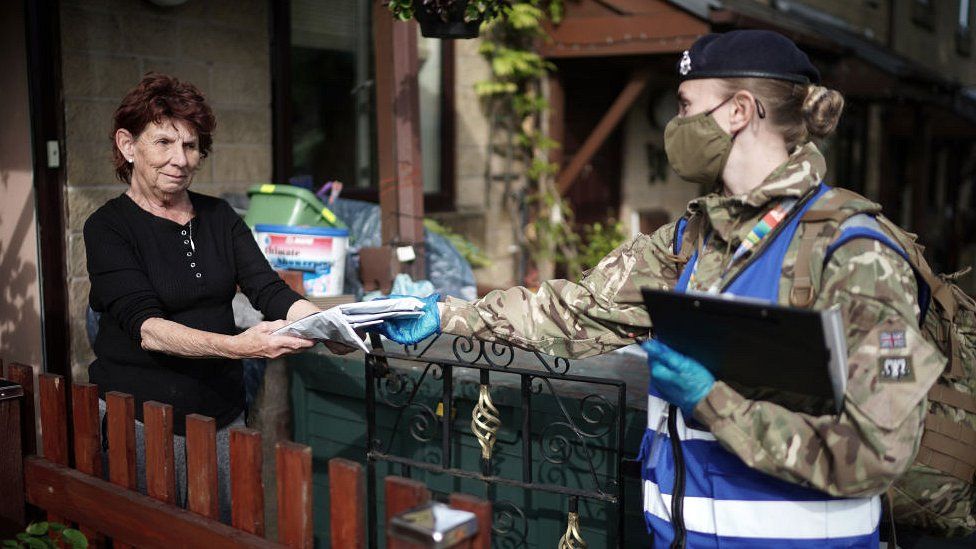 army officer in mask hands surge testing kit to woman