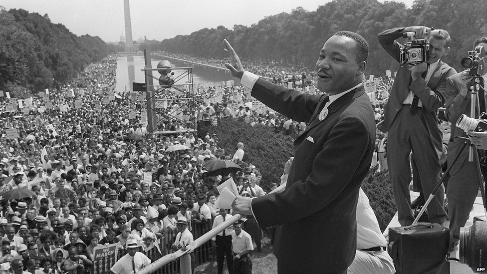 Лидер гражданских прав Мартин Лютер Кинг (в центре) машет рукой сторонникам 28 августа 1963 года в торговом центре в Вашингтоне, округ Колумбия