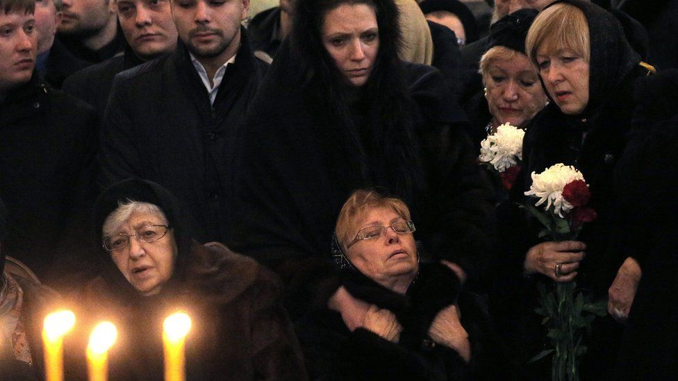 Marina Karlova (seated, R), the widow of killed Russian ambassador to Turkey, Andrei Karlov, and his mother Maria (seated, L) are surrounded by mourners (22 Dec)
