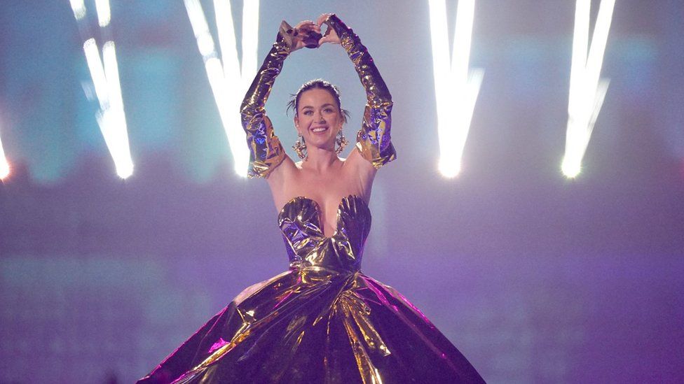 Katy Perry holding her arms up and wearing a golden gown