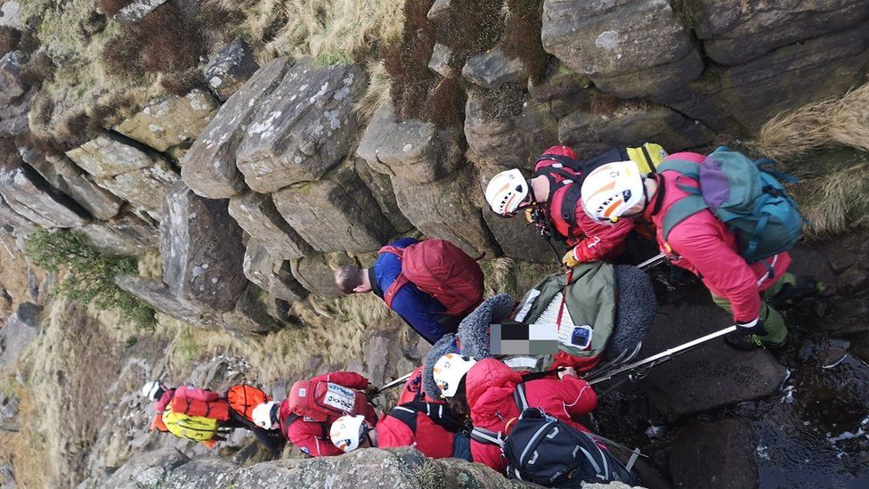 The Edale Mountain Rescue Team is pictured with a casualty on a stretcher during a rescue on Monday