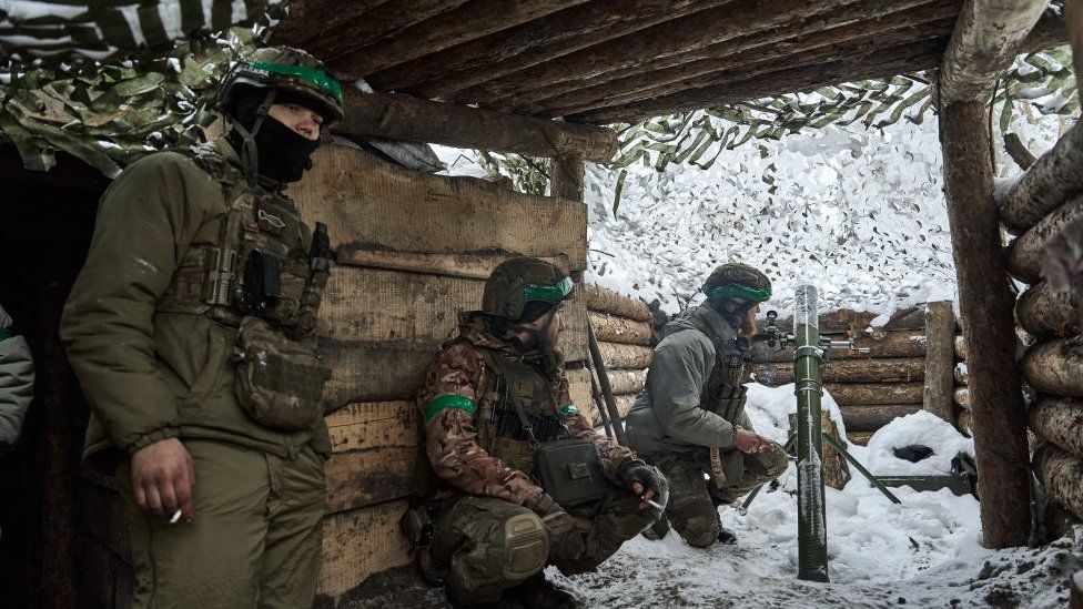 Ukrainian soldiers seen in a snowy dugout. One is manning a mortar.