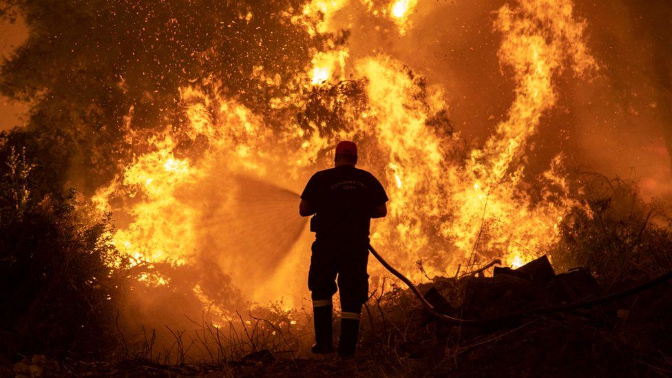 A firefighter tries to extinguish a wildfire burning in the village of Pefki, on the island of Evia, Greece