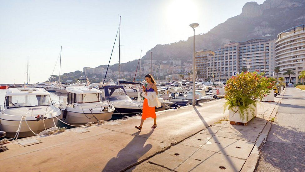 Vanesa, walking along a marina in front of a series of boats in Monaco