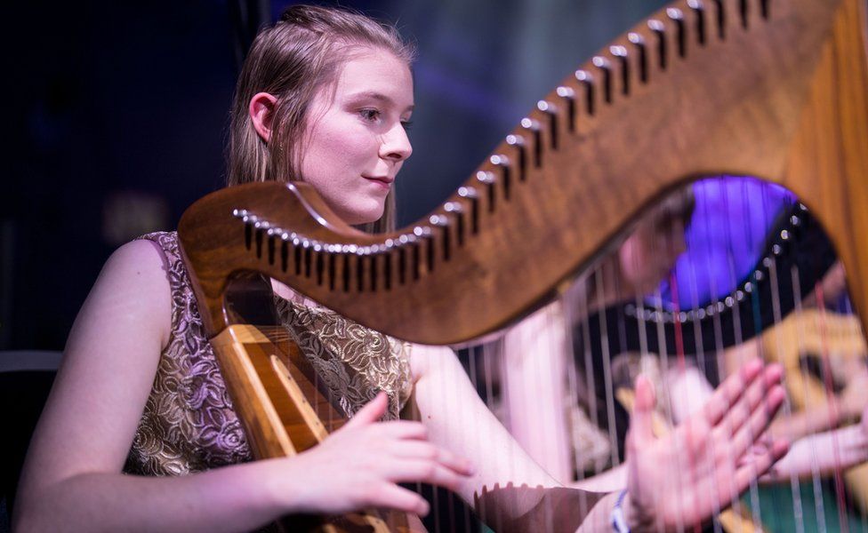 A young woman plays a harp as part of the orchestra