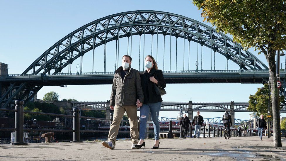 Couple wearing masks walking along Newcastle Quayside with Tyne Bridge in the background