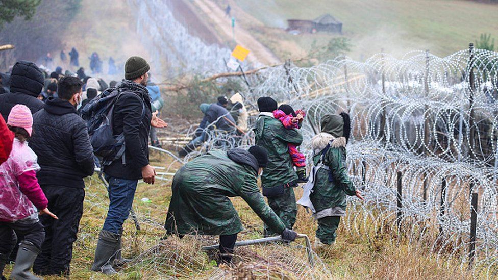 Migrants stand near a barbed-wire fence