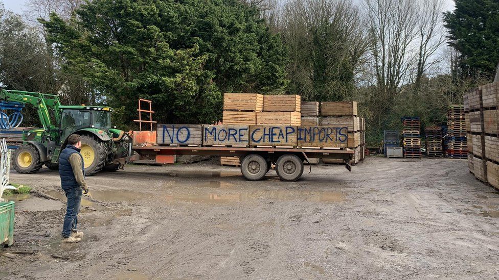 A tractor with a trailer carrying wooden crates spray-painted with the words: "No more cheap imports"