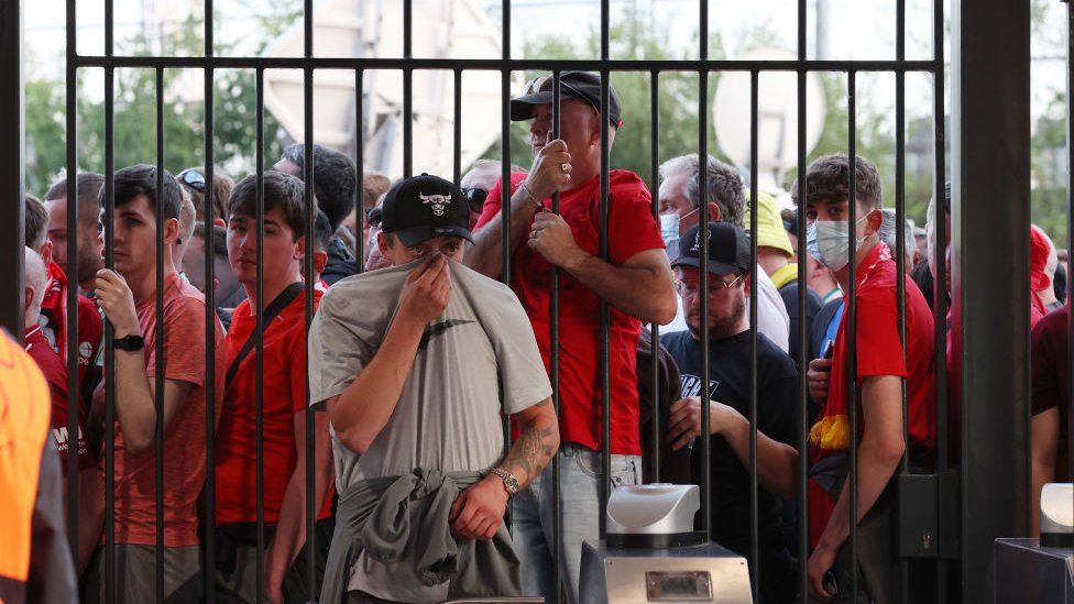 Liverpool supporters look through the closed gates of the Stade de France, some holding their tops over their noses and mouths after tear gas was used on them