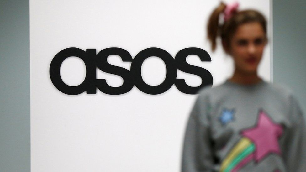 A model walks on a catwalk with an Asos logo in the background