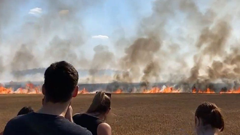 Locals watch on as the fire spreads cross a field